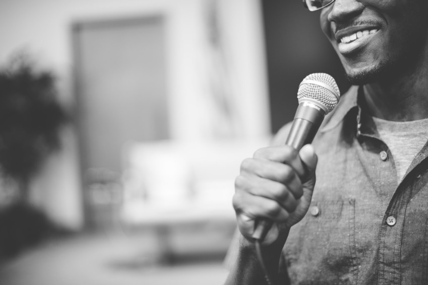 Greyscale shot of a happy African-American male talking on the microphone at the church